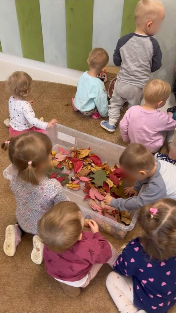 Maluchy przeglądają kolorowe jesienne liście w sensorycznym pudełku – żłobek w Starym Ochędzynie