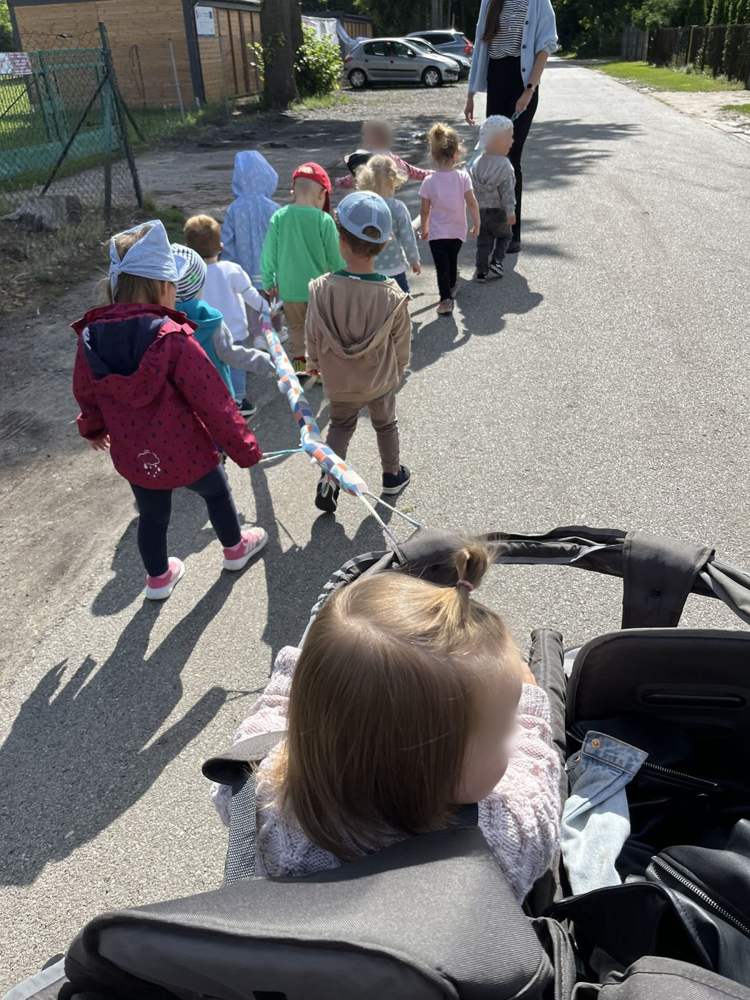 Spacer przedszkolaków i żłobkowiczów z Cieszęcina – dzieci idą razem trzymając kolorowy wąż spacerowy